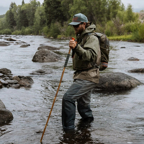 Man fishing in a river surrounded by trees and rocks