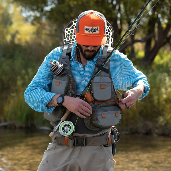 Man in outdoor setting with fishing gear and orange cap