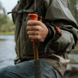 Person holding a wading staff by a river with a blurred natural background