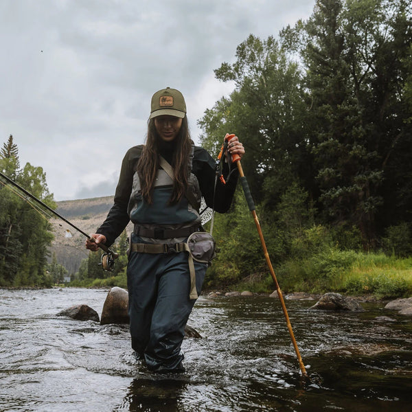Person fly fishing in a river with a wading staff surrounded by trees