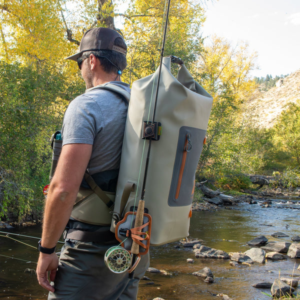 Man fishing by a river with a large backpack on