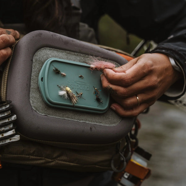 Person holding a fly fishing lure box with flies and a hook.