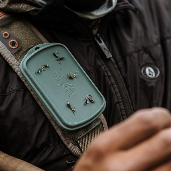 Person in camouflage attire with a green device on a strap, possibly related to hunting or outdoor activity.