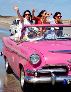 Old car with girls waving while driving along the malecon. Down town Havanna.