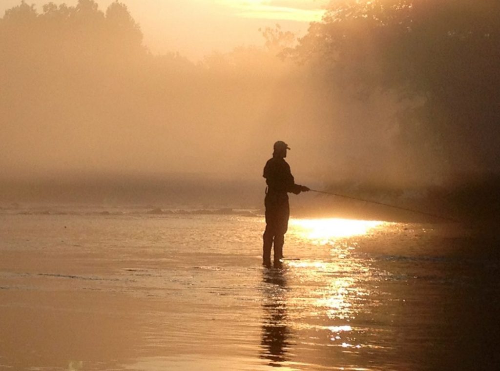 An angler from Sachem's pass stands in the river while the sun rises.